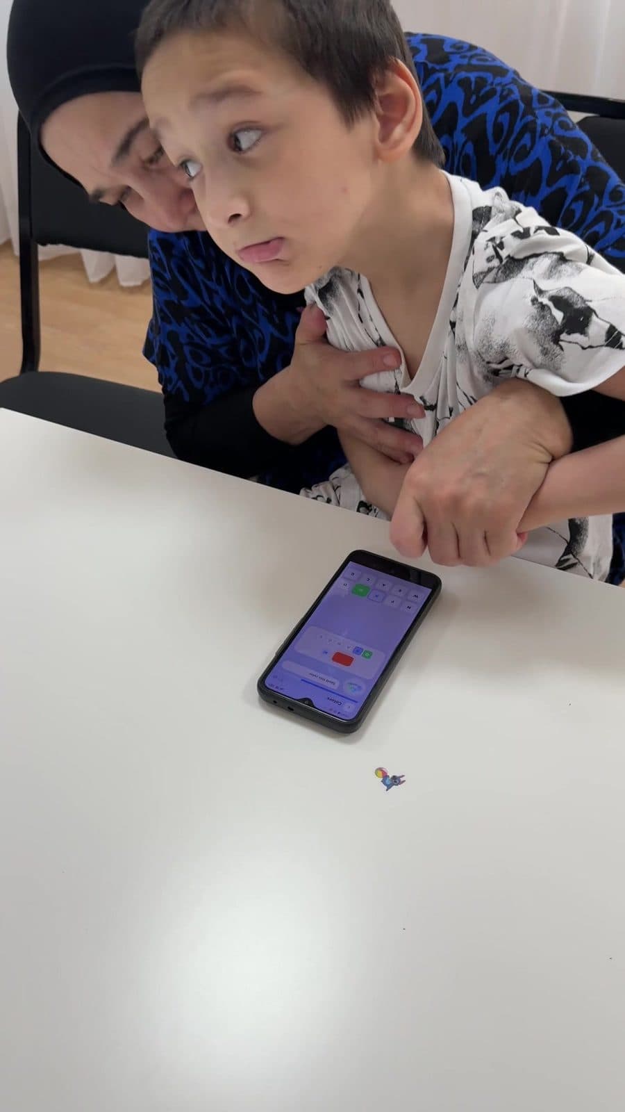 A child closely supported by a caregiver while using FlexiKeys on a phone